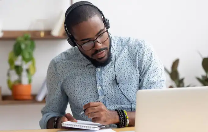 A man wearing headphones and taking notes