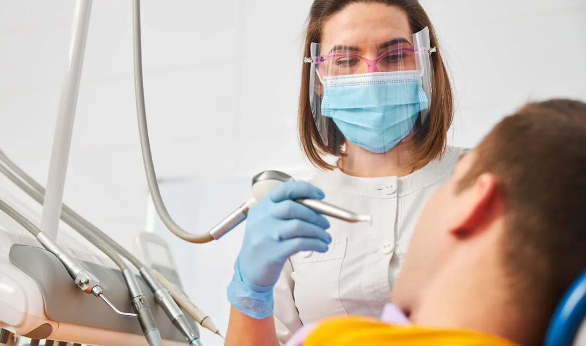 a dental assistant wearing a mask and holding a dental instrument over a patient in a chair