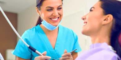 a dental assistant smiling at a patient in a dental chair while holding dental instruments