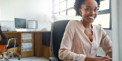 a healthcare accounting professional smiling while working on a computer after completing a healthcare accounting degree program