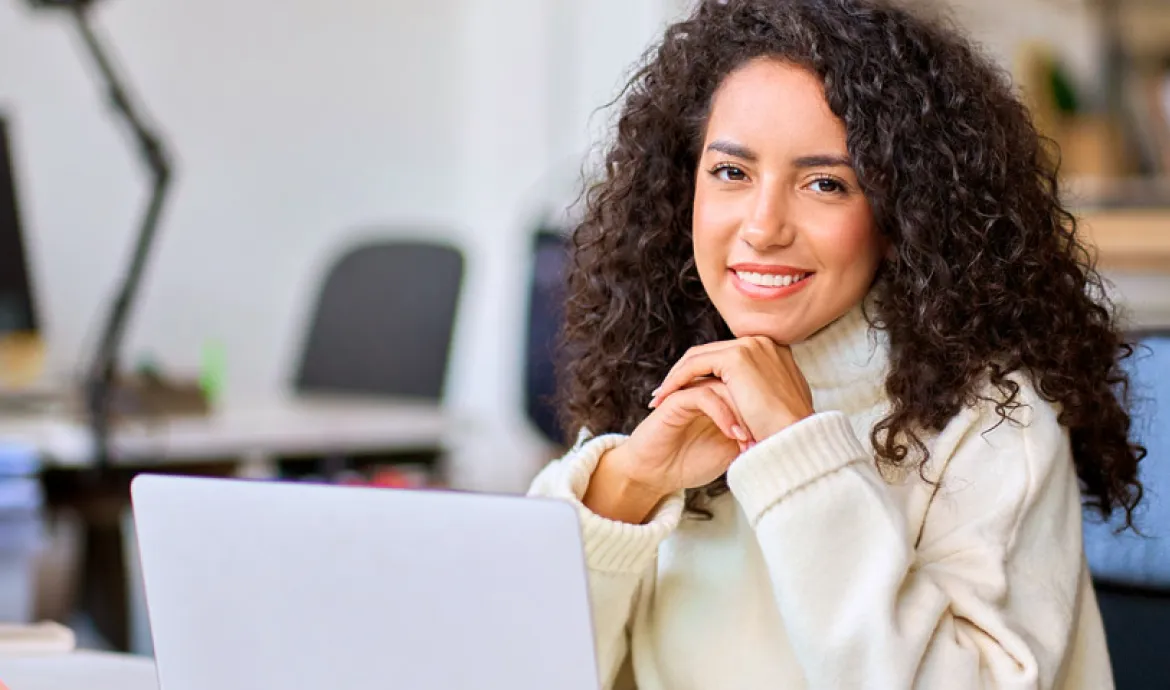 a healthcare accounting worker smiling while sitting at a desk in front of a laptop