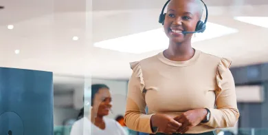 a healthcare management professional standing in and office while smiling and wearing a headset after completing healthcare management training