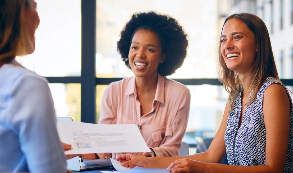 two healthcare management workers smiling as they discuss paperwork with a colleague