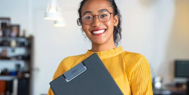 a healthcare management grad smiling while holding a clipboard at her first job