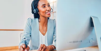 a health information management professional taking notes while talking on a headset and looking at a computer screen