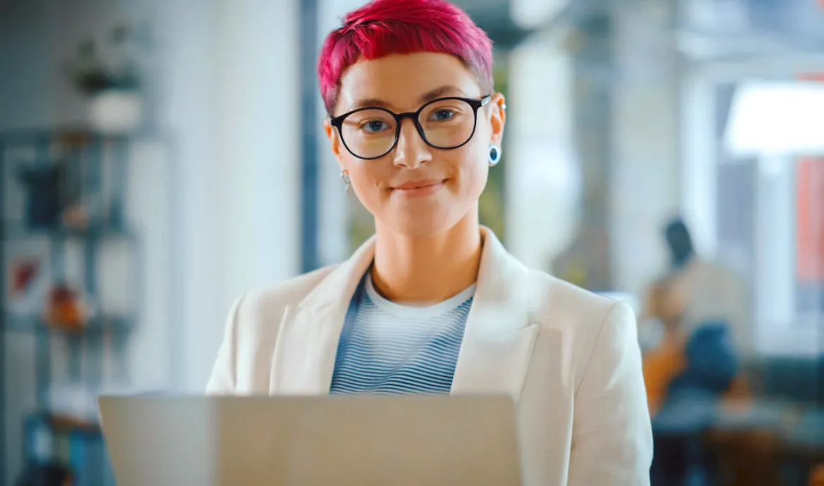 a health information technician smiling while standing in front of a computer after completing a health information management course