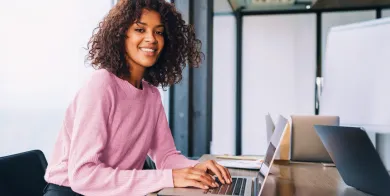 a medical administrative assistant student smiling while doing online coursework on her laptop