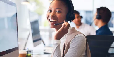 medical biller and coder grad smiling while talking on a headset and working at a computer