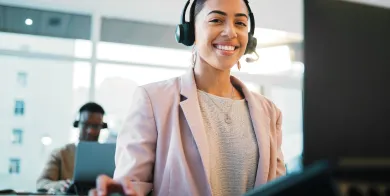 a medical office and billing specialist sitting in front of computer and smiling with one hand on a mouse and wearing a headset