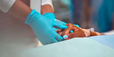 gloved hands of a patient care technician holding a patient’s hand to provide comfort