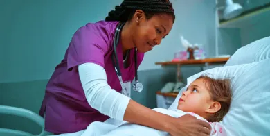 a patient care technician pulling covers up to the chin of a pediatric patient lying in bed