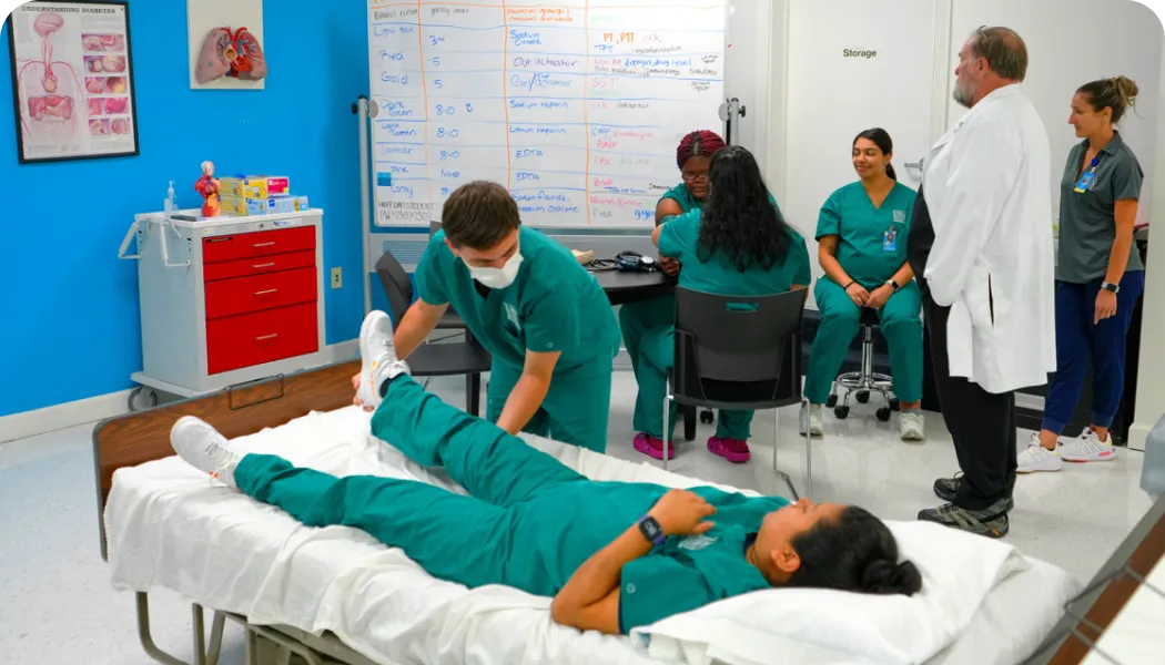 healthcare student practicing patient care on another student who is lying in a hospital bed